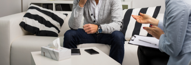 kaksi ihmistä istuvat, toinen nojaa polveensa ja toinen pitää kirjoituslehtiötä sylissään