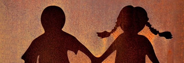 Seinään syntyvässä varjossa kaksi ihmistä pitävät toisiaan kädestä kiinni