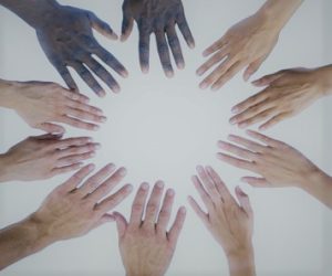 Viiden ihmisten kädet muodostavat ympyrän, jossa valo keskellä