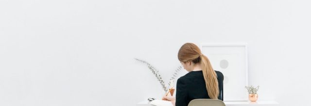 Nainen yksin töissä pöydän äärellä valkoisella taustalla