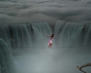 Nainen kävelee ja tasapainottelee lankaa pitkin vesiputouksen yläpuolella