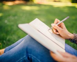 Nainen kirjoittaa kirjaan istumalla ruoholla