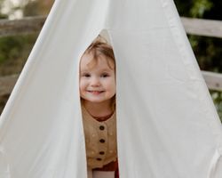 Tyttölapsi kurkkii valkoisesta teltasta