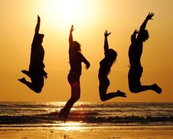 Neljä ihmistä hyppivät ilmaan rannalla auringonlaskun alla