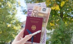 Nainen pitää saksalaista passiaan ilmassa, jonka päällä on miniatyyrilentokone ,ja jonka sisällä on euroseteleitä.