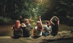 5 nuorta naista istuvat puurungon päällä keskellä viidakkoa.