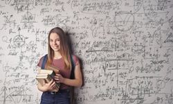 Nainen nojaa seinään, johon on kirjoitettu paljon monimutkaisia matemaattisia kaavoja. Kädessään hän pitää kirjoja.