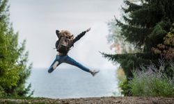 Nainen hyppää ilmaan reppunsa kanssa luontomaisemassa