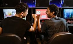 Kaksi nuorta miestä pelaavat yhdessä pelitietokoneilla ja laittavat kätensä yhteen ystävyyden merkeissä