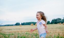 Tyttö juoksee pellolla nauraen