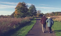 Vanhempi mies ja nainen tukevat toisiaan, kun kävelevät puistopolkua pitkin