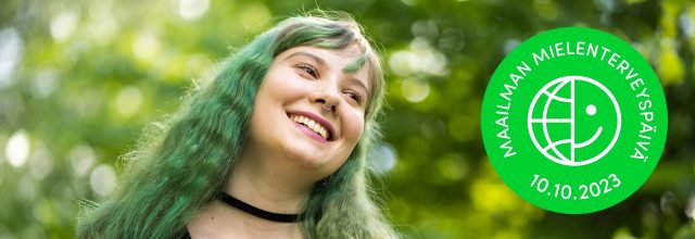 Vihreähiuksinen, nuori hymyilevä nainen lähikuvassa. Taustalla vihreä puistomaisema.